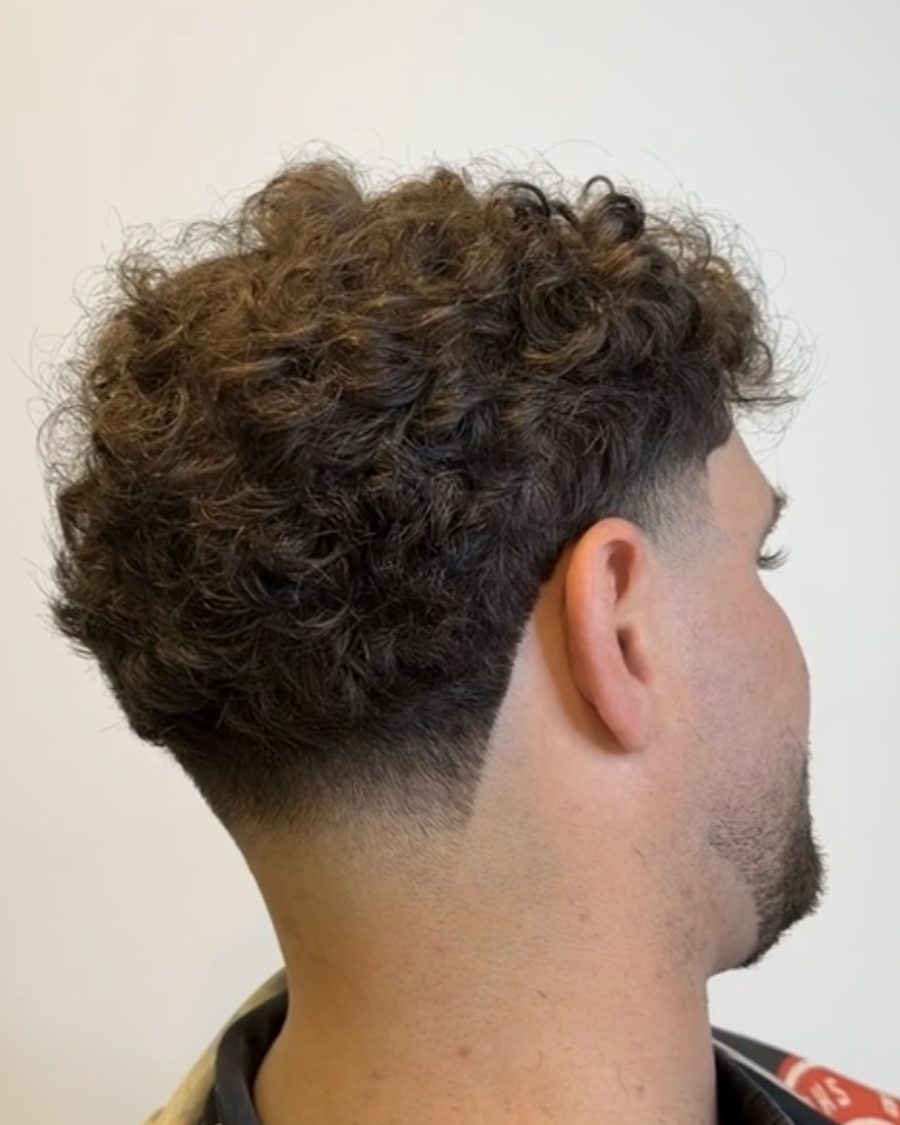 Curly taper fade with a clean neckline, cut at Studio K